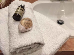 A bathroom with a white towel, a bottle of shower gel, and a bar of soap on a sink. - Les Aiguières en Provence (Suze-la-Rousse)
