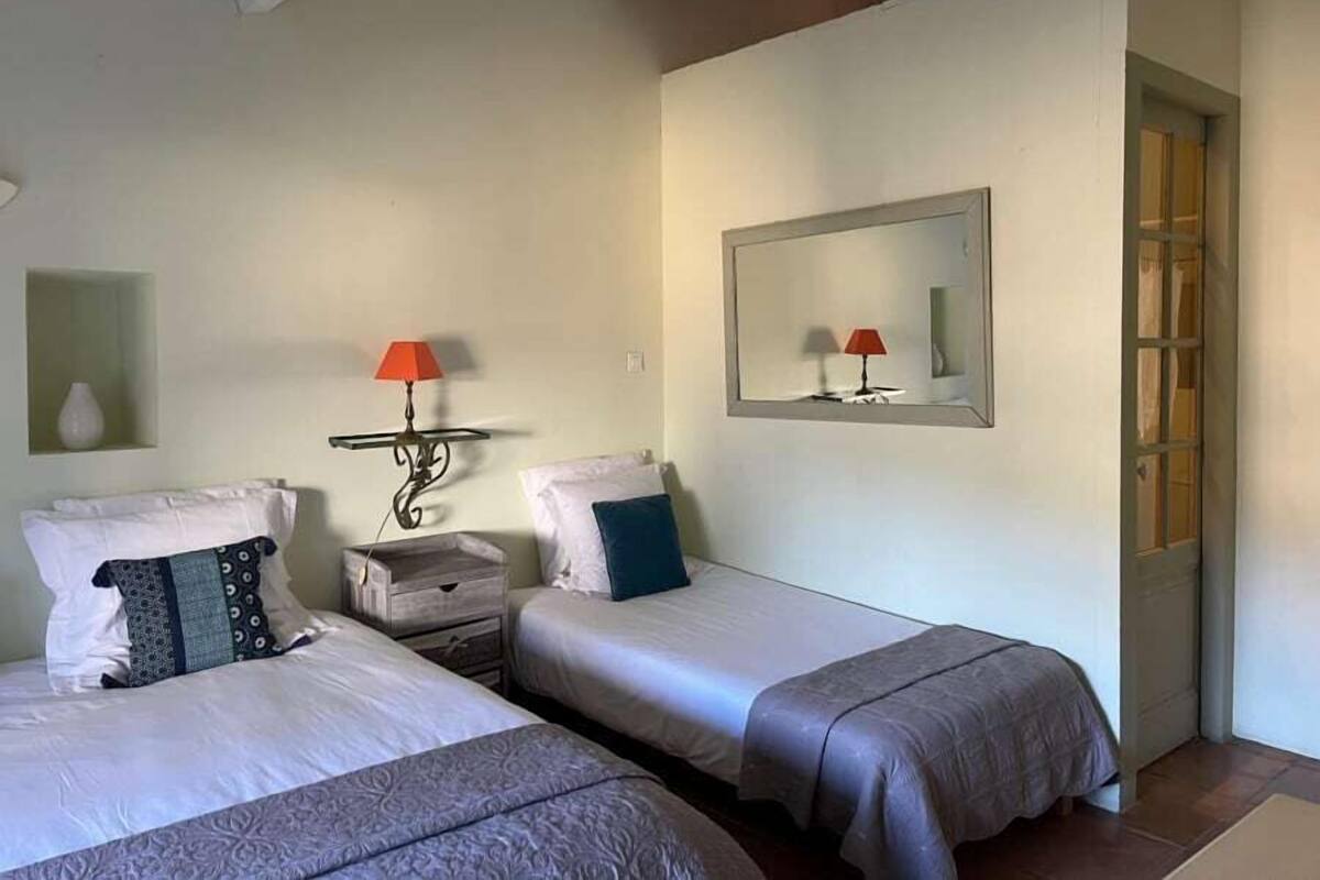 Camera d'albergo con due letti, un comodino, una lampada, uno specchio e un tavolino.