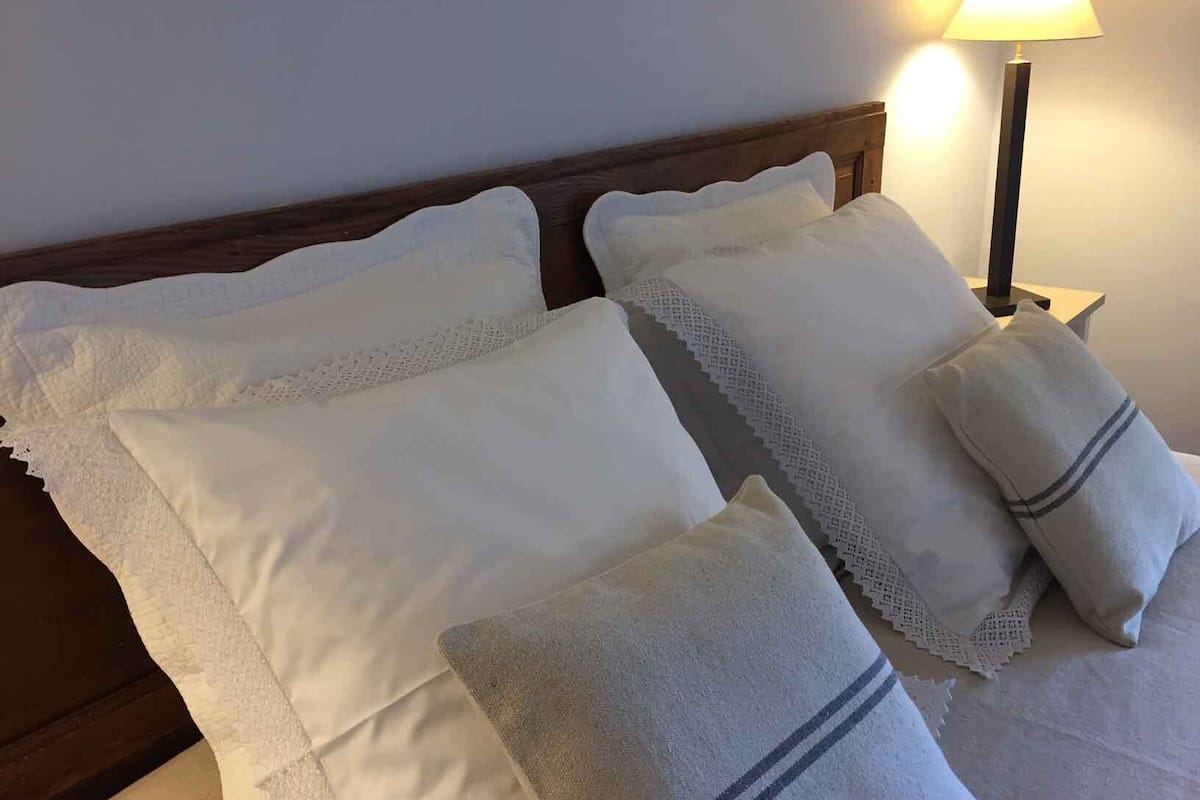 Un letto rifatto con lenzuola bianche e due cuscini, una lampada da comodino e una testiera in legno.