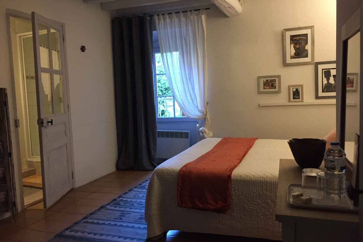 Una camera da letto con un letto, un comodino, una finestra con tende e quadri appesi al muro.