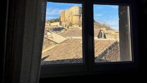 A view through a window of a building with a large, historic structure in the background. - Les Aiguières en Provence (Suze-la-Rousse)