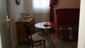 Et lille, hyggeligt værelse med skrivebord i træ, stol, lille bord, rød sofa og et vindue med gardiner.