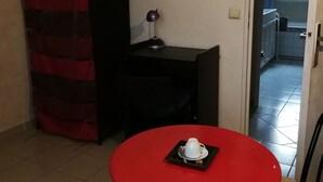 Et lille rum med et rødt bord, en sort stol, en hvid kop og en sort lampe på et lille bord.