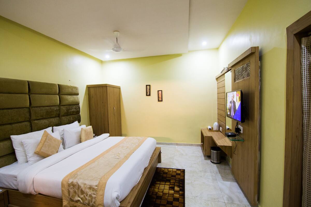 Habitación de hotel con una cama grande, un cabecero de madera, un televisor en la pared y un pequeño mueble de madera.