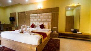 Een hotelkamer met een groot bed, een houten hoofdbord, een televisietoestel, een spiegel en een houten bankje.
