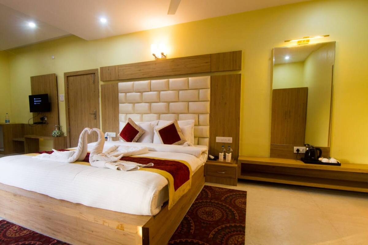 Habitación de hotel con una cama grande, cabecera de madera, televisión, espejo y banco de madera.