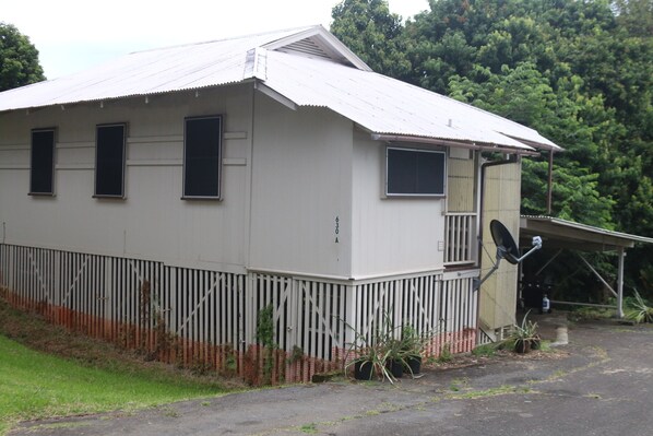 A single-story building with a corrugated metal roof, a fenced yard, and satellite dishes. - Wainaku Camp Home (Hilo)