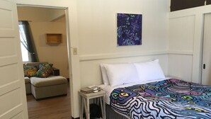 Un dormitorio con cama, mesita de noche, silla y puerta que da a otra habitación.