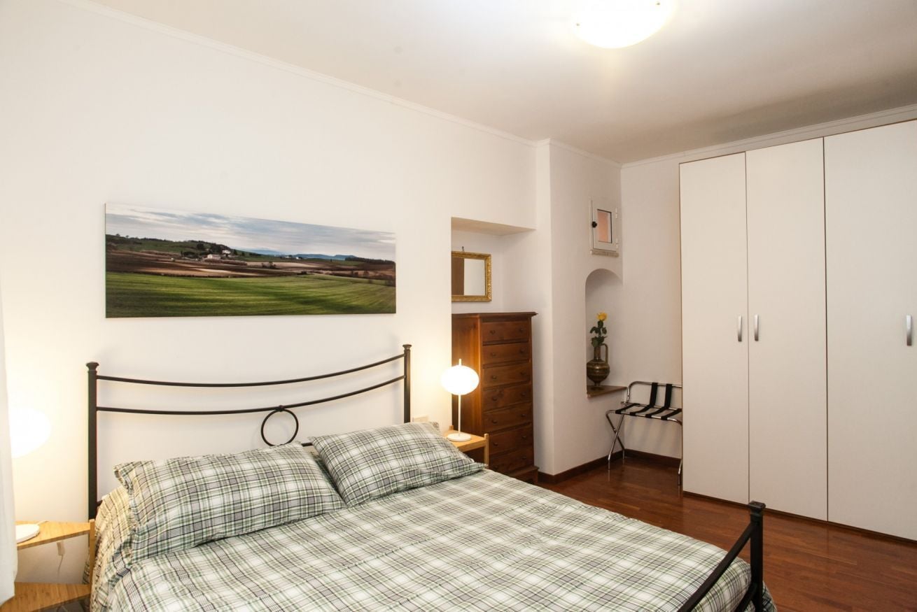 A bedroom with a bed, a nightstand, a lamp, a wardrobe, and a painting on the wall.