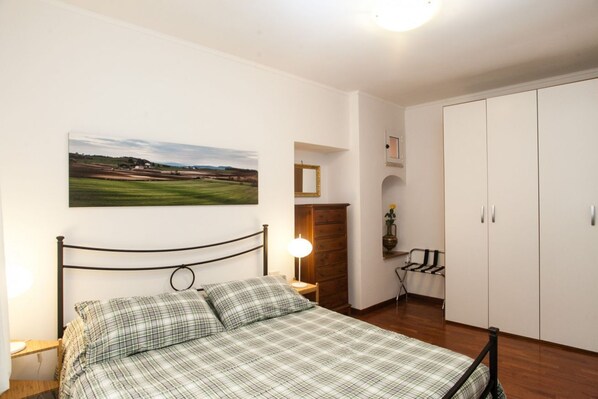 A bedroom with a bed, a nightstand, a lamp, a wardrobe, and a painting on the wall.