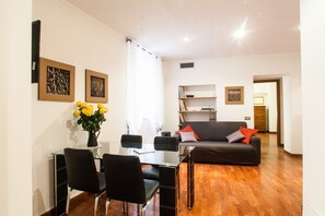 A modern living room with a glass dining table, black chairs, a dark sofa with cushions, and a vase of yellow flowers. - Casa Zeffiro, two minutes walk from Trevi Fountain (Roma)