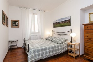 A bedroom with a bed, a bedside table with a lamp, a dresser, and two framed pictures on the wall.