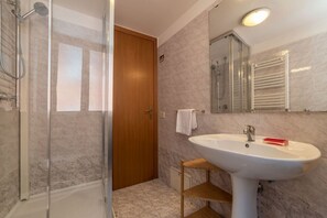 A bathroom with a glass-enclosed shower, a wooden door, a white sink, and a mirror above it.