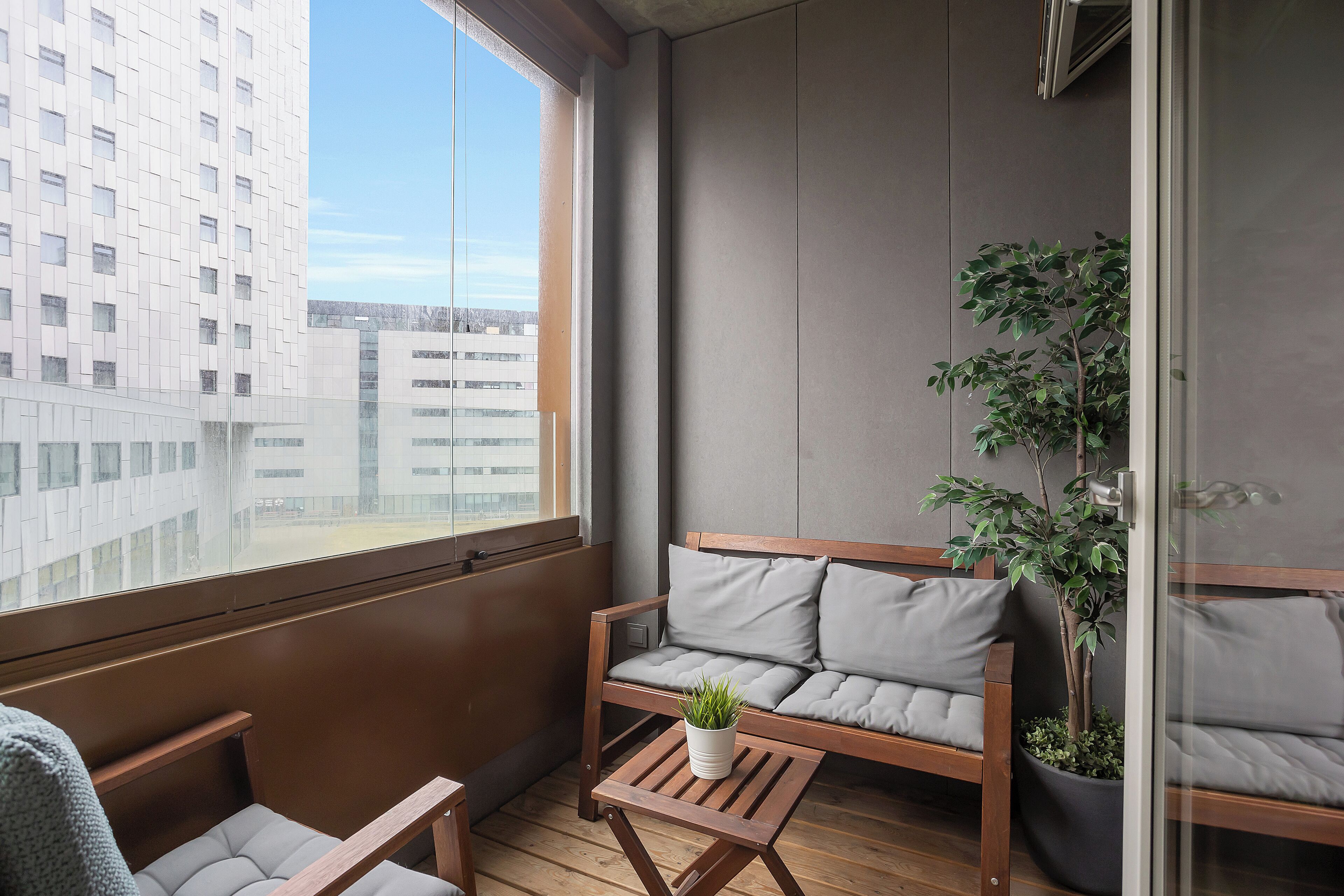 Un balcón con un sofá de madera, una mesa pequeña con una planta y otra planta en maceta junto al sofá.