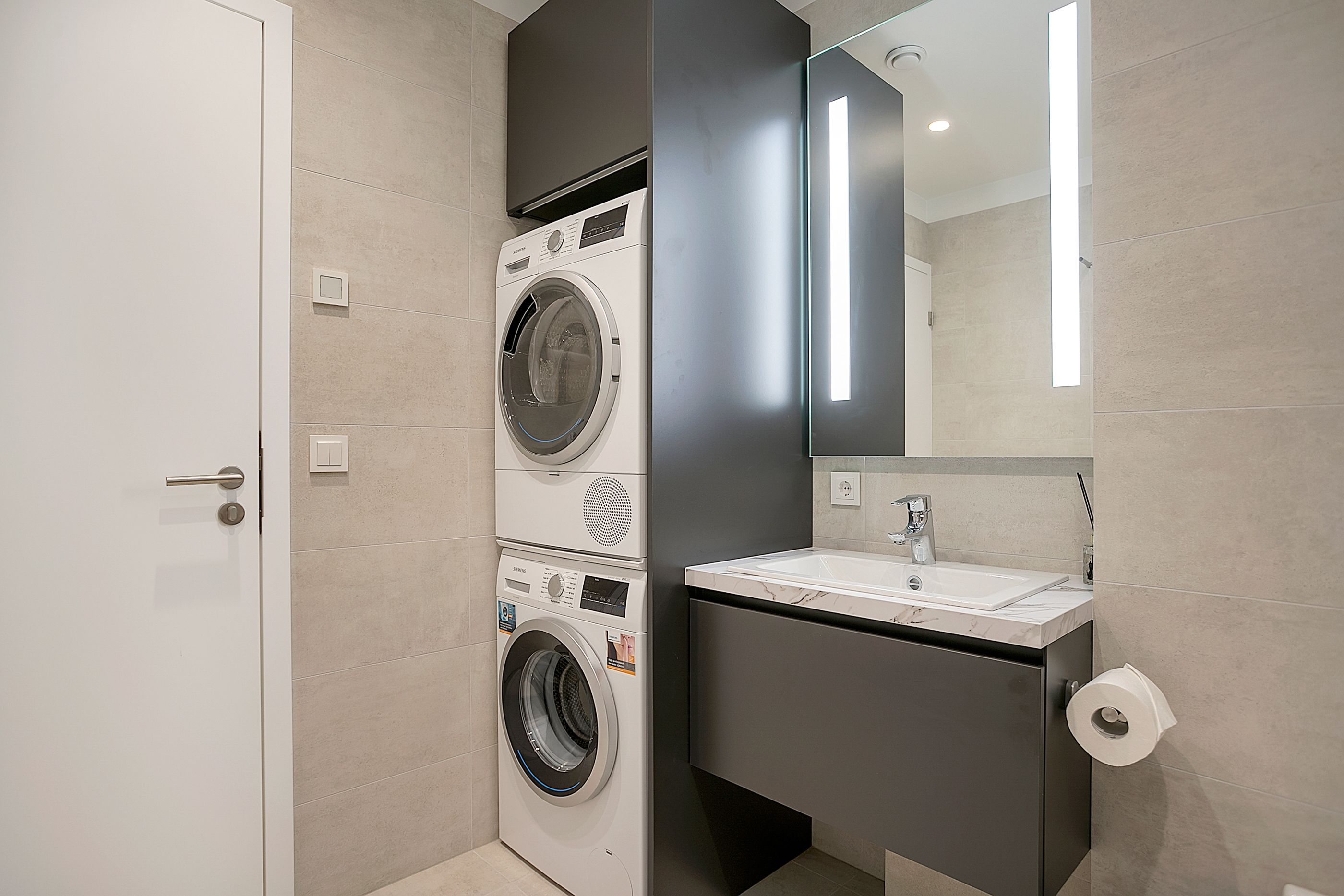 A modern bathroom with a washing machine, a sink, and a toilet.