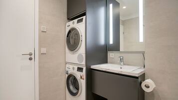 A modern bathroom with a washing machine, a sink, and a toilet.