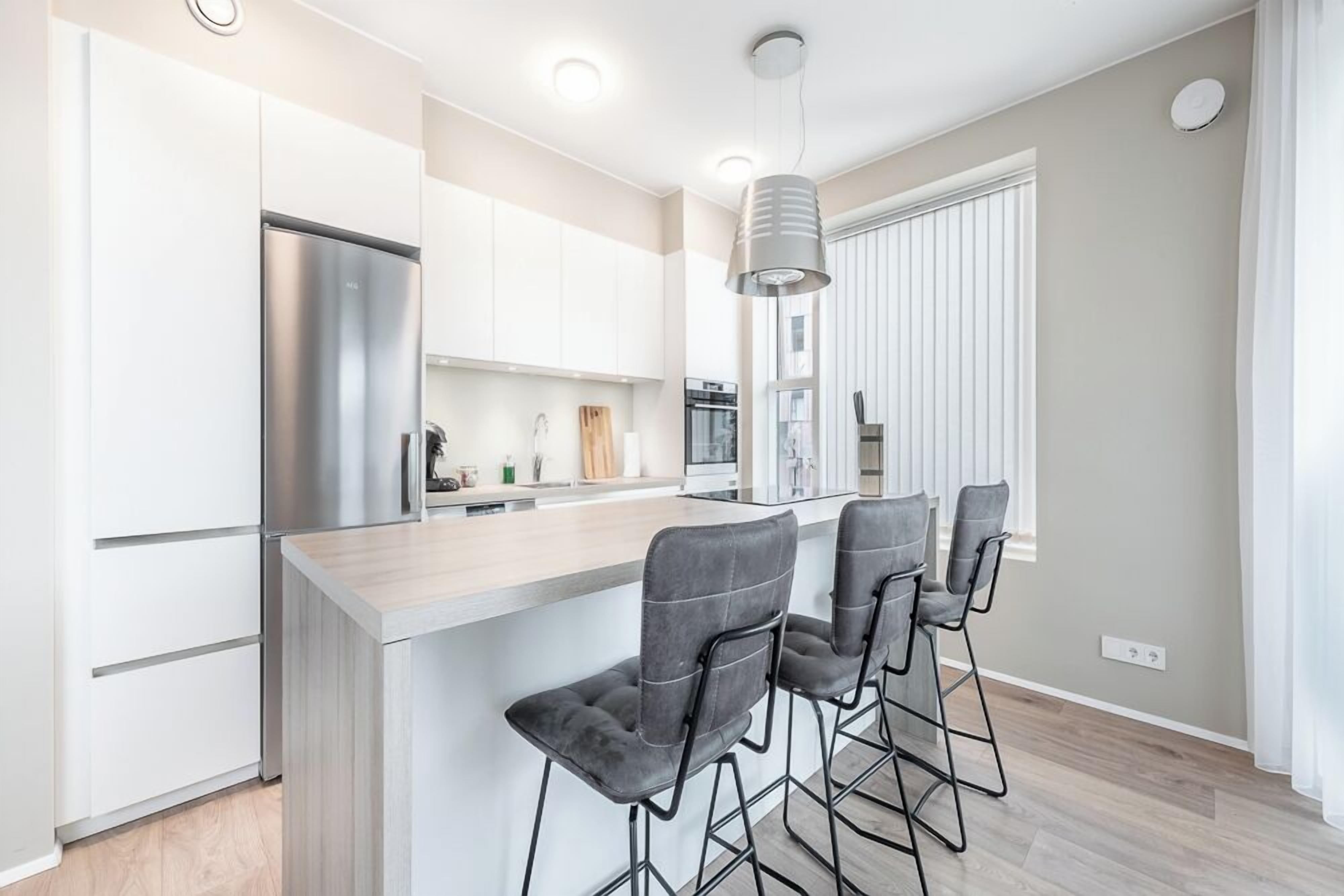 A modern kitchen with white cabinets, a stainless steel refrigerator, and a bar area with grey stools.