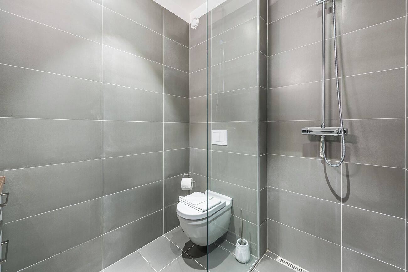 A modern bathroom with grey tiles, a glass shower enclosure, a toilet, and a handheld showerhead.