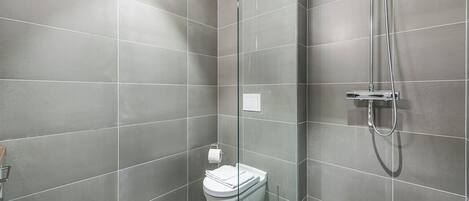 A modern bathroom with grey tiles, a glass shower enclosure, a toilet, and a handheld showerhead.