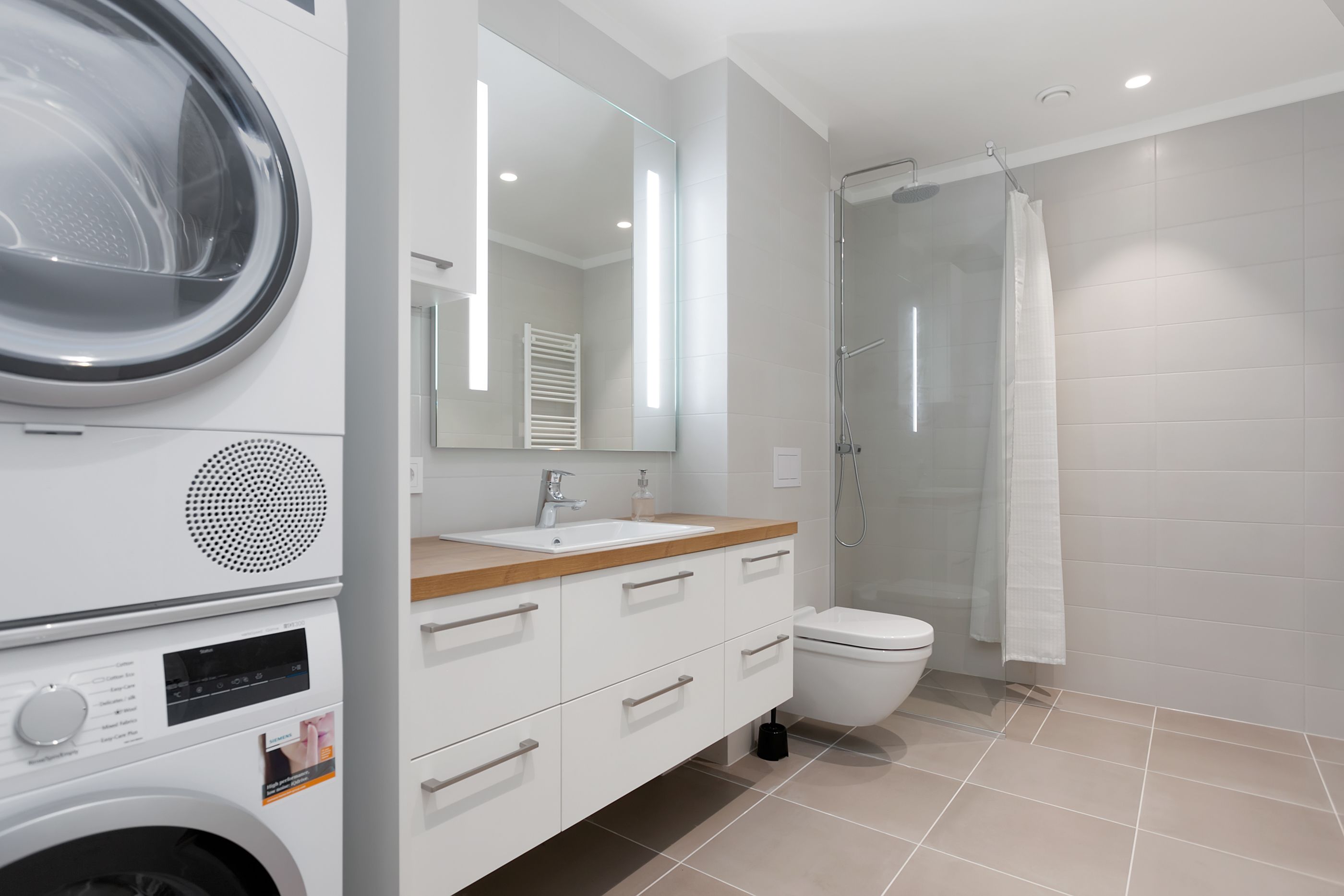 A modern bathroom with a washing machine, a sink, a toilet, and a glass shower enclosure.