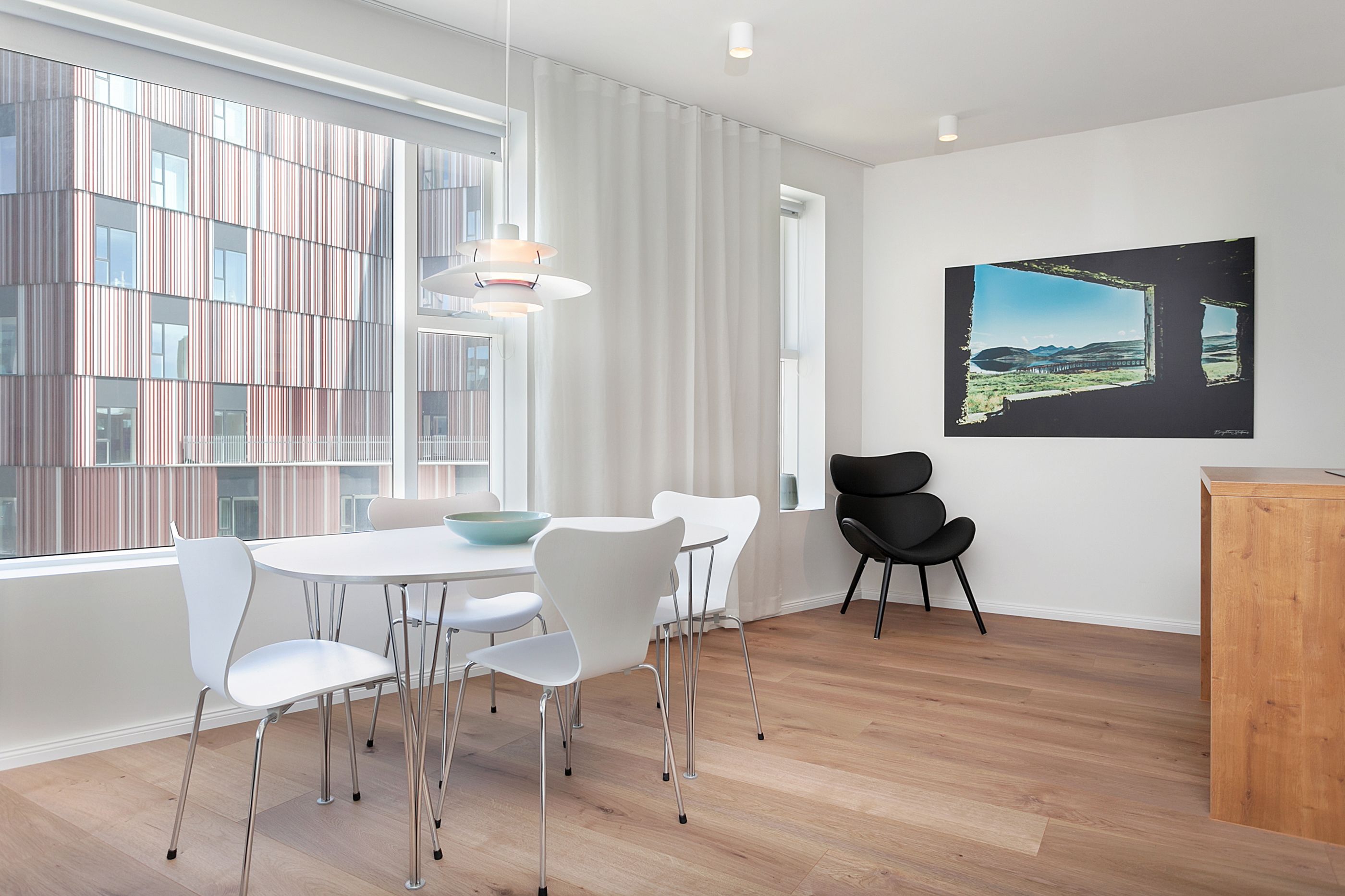 A modern dining area with a white table and chairs, a wooden floor, and a large window with curtains.