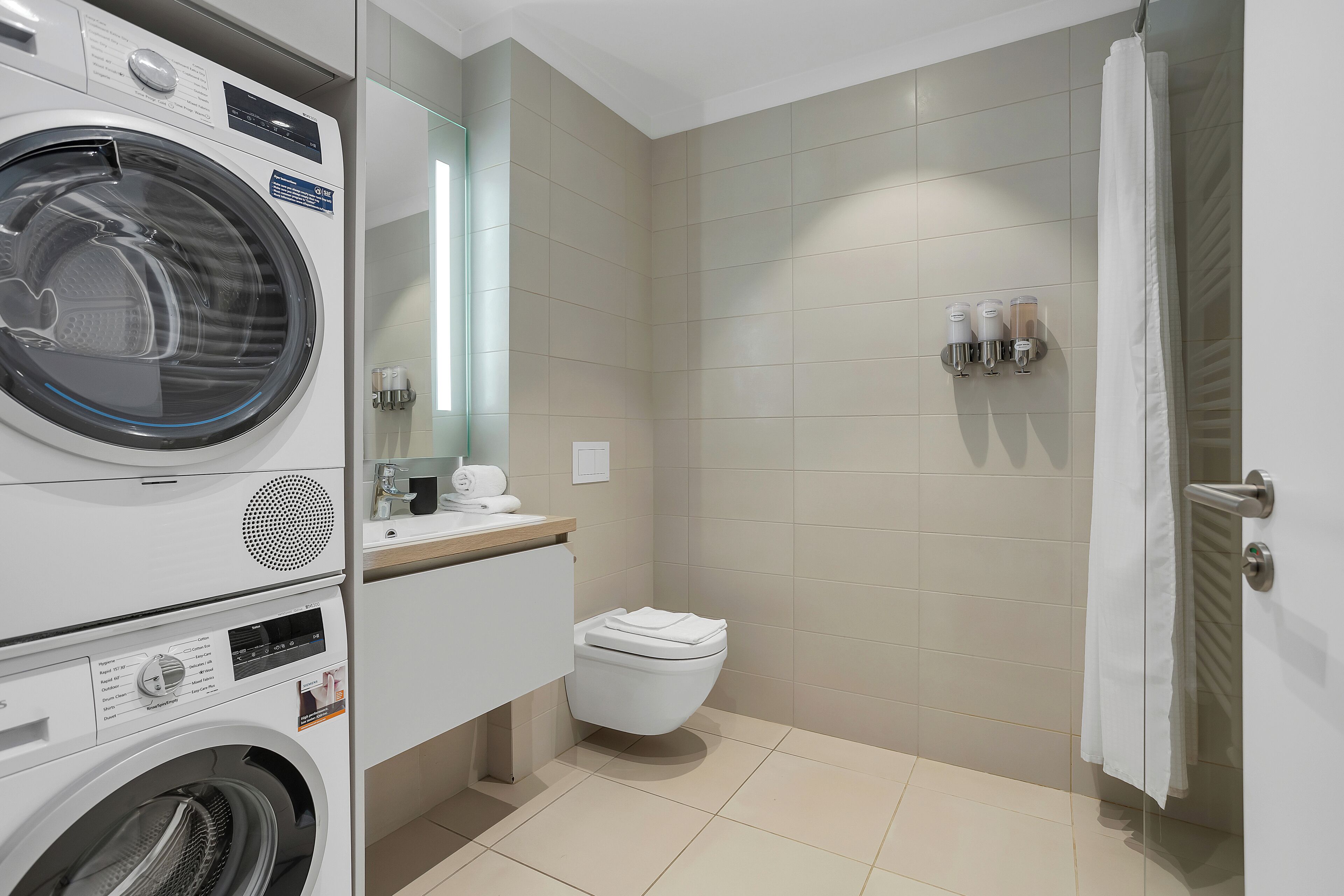A modern bathroom with a washing machine, toilet, and shower area.