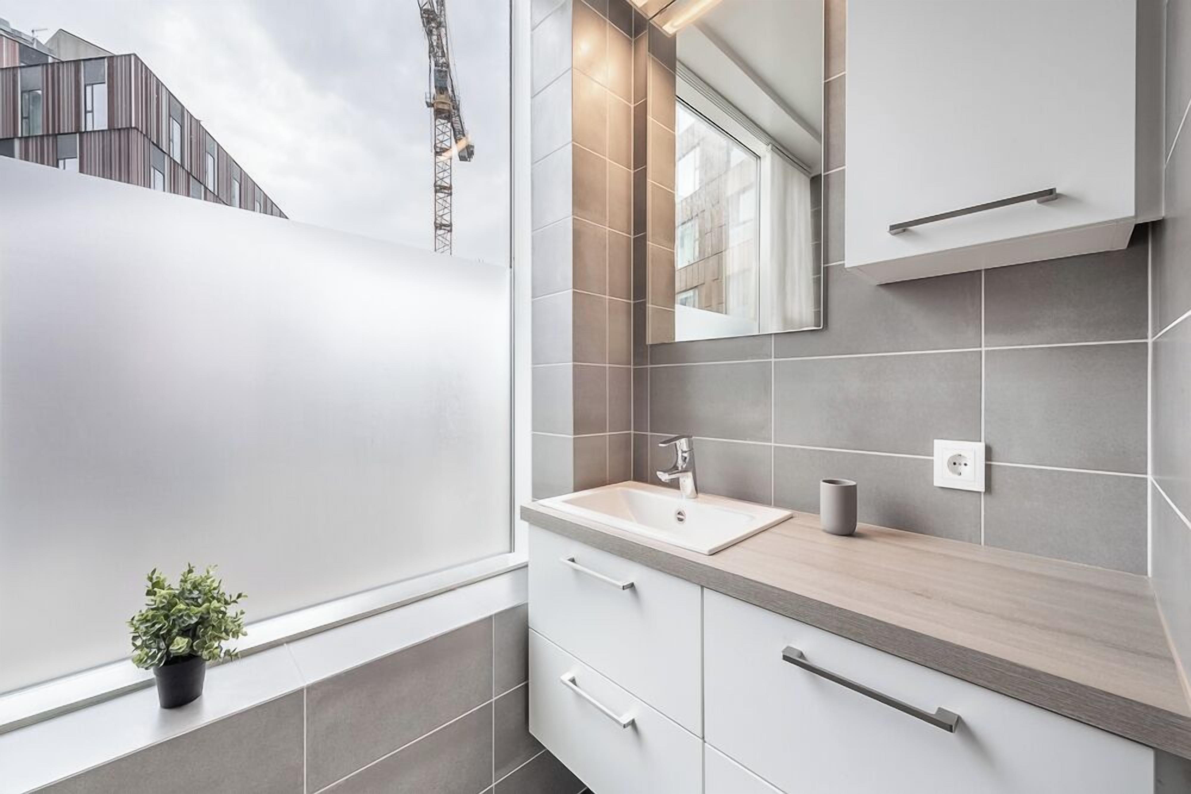 Une salle de bain moderne avec une grande fenêtre, un lavabo et un miroir.