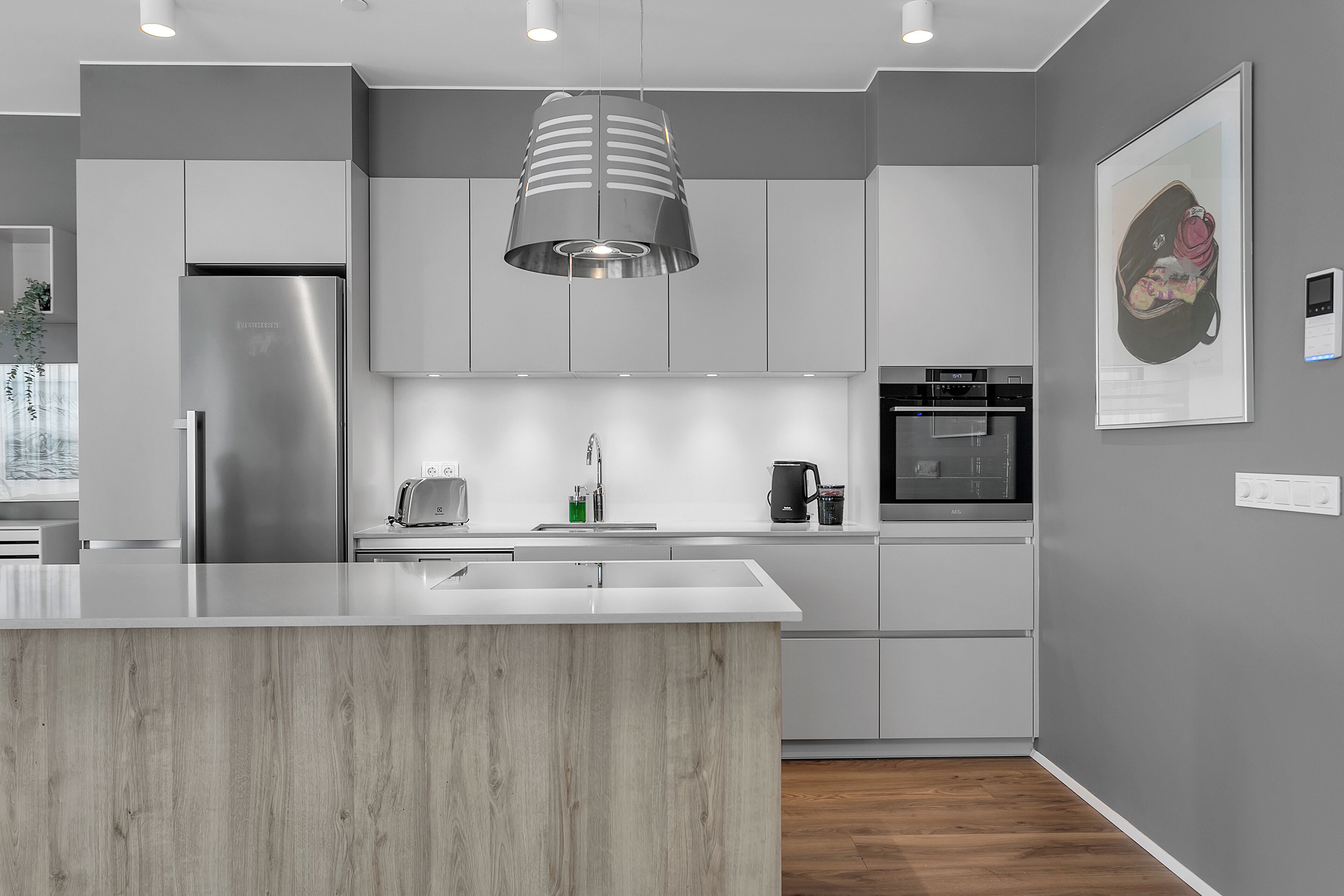 Een moderne keuken met een centraal eiland, roestvrijstalen apparatuur en een hanglamp.