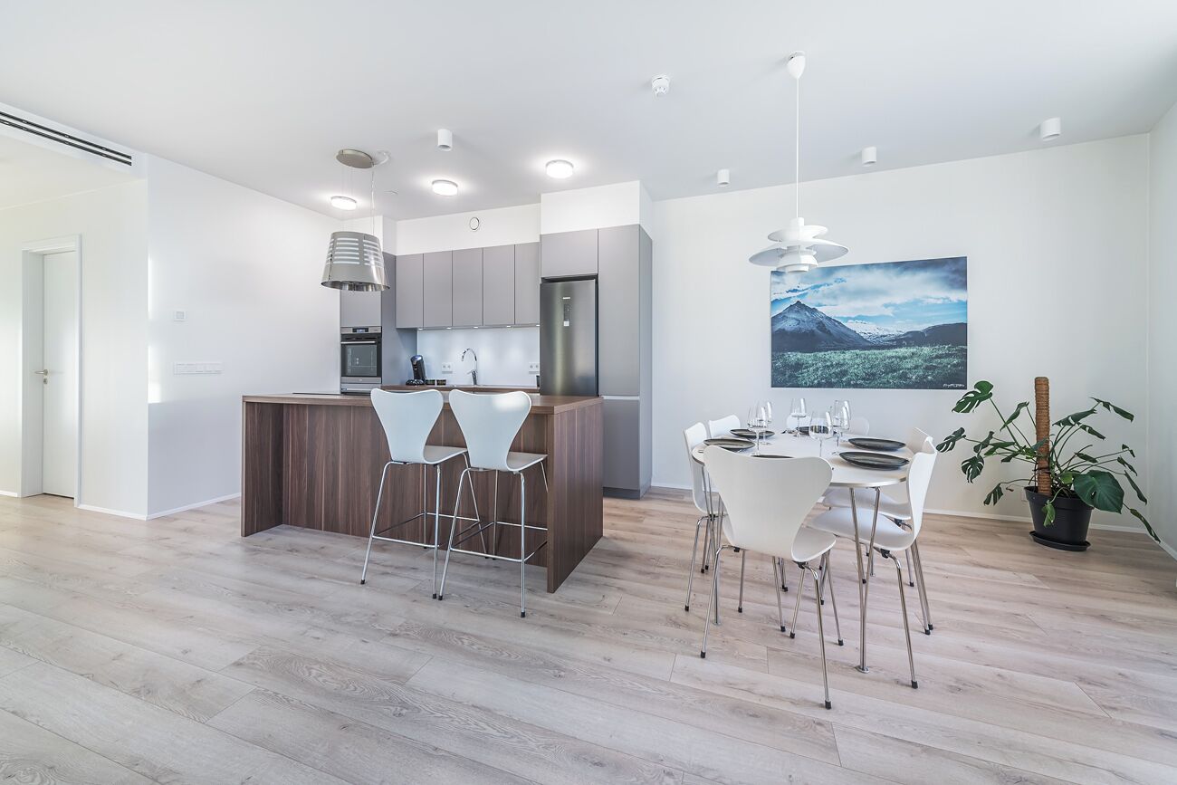 Een moderne keuken met grijze kastjes, een centraal eiland en witte stoelen.