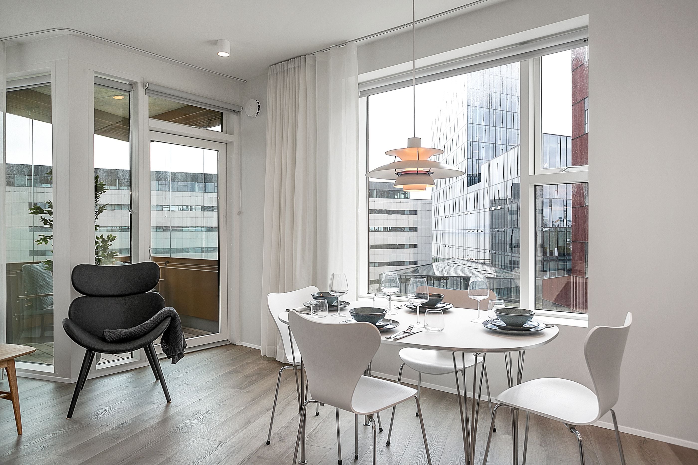 Un comedor moderno con una mesa redonda, sillas blancas y un amplio ventanal con vista a un edificio.
