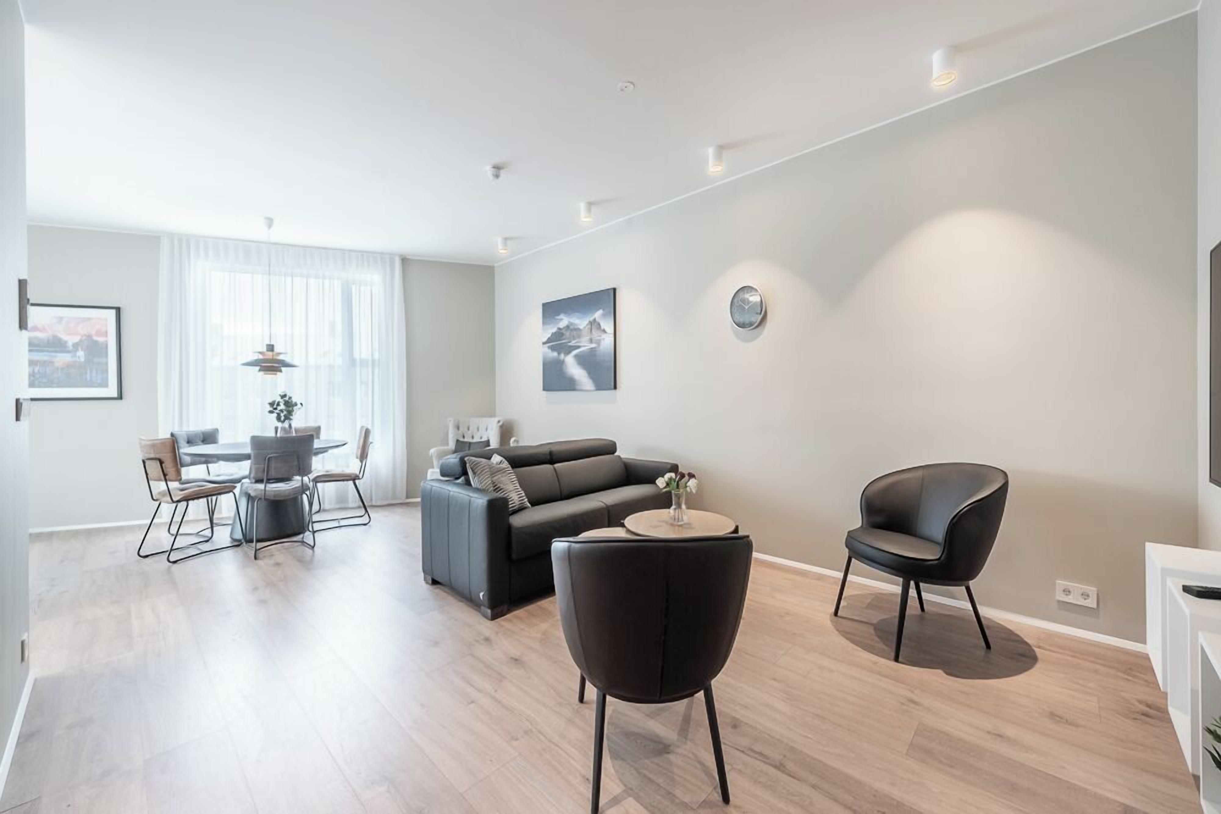 A modern living room with a grey sofa, a dining table with chairs, and a black armchair.