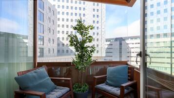 Un balcón con dos sillas de madera, una planta en maceta y vistas a edificios modernos.