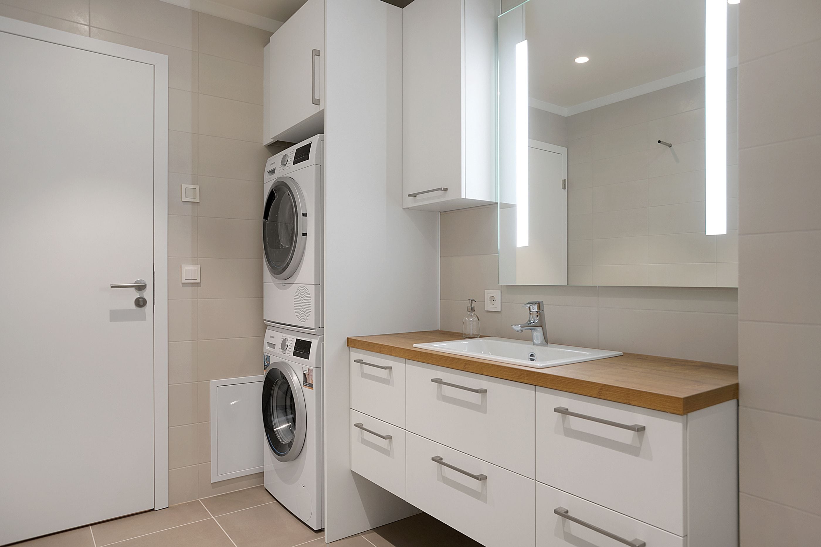 Un baño moderno con lavadora y secadora apiladas, un lavamanos con encimera de madera y un espejo grande.