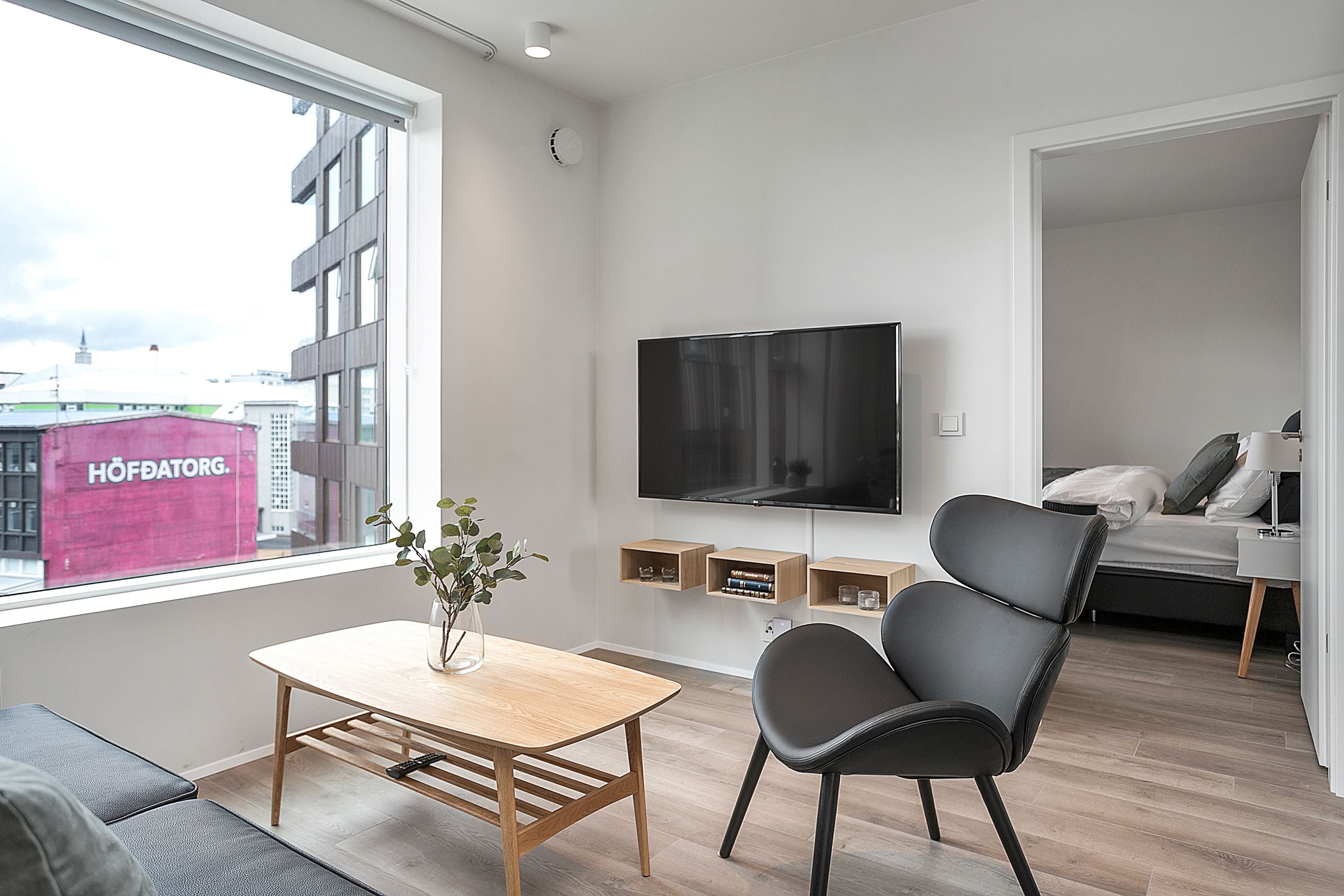 A modern living room with a large TV, a wooden table, and a comfortable chair.
