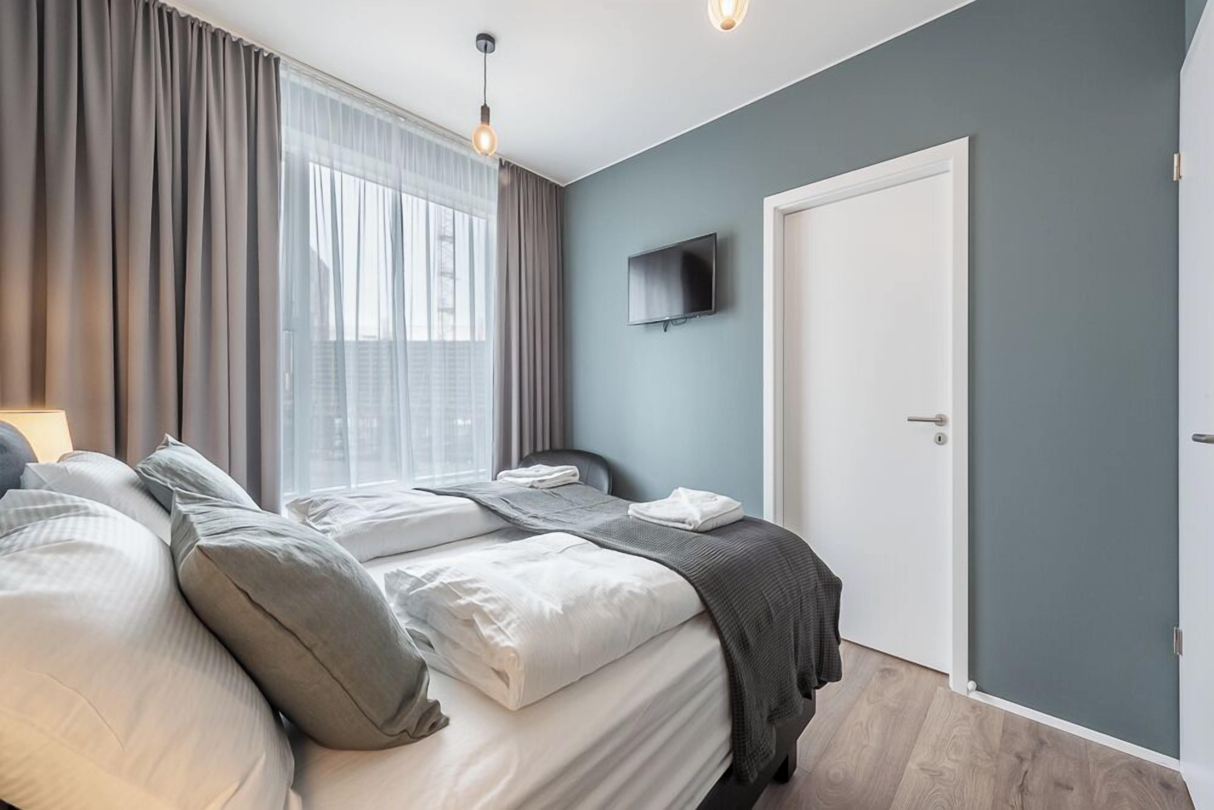 A bedroom with a bed, a TV mounted on the wall, and a door.