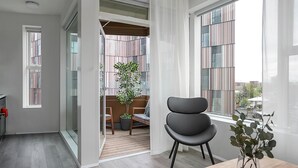 A modern interior with a dining area, a large window with curtains, and a view of a building outside. - Sif Apartments by Heimaleiga (Reykjavik)