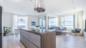 A modern apartment with a central kitchen island, a dining area, a living room with a sofa and armchairs, and large windows offering a city view. - Sif Apartments by Heimaleiga (Reykjavik)