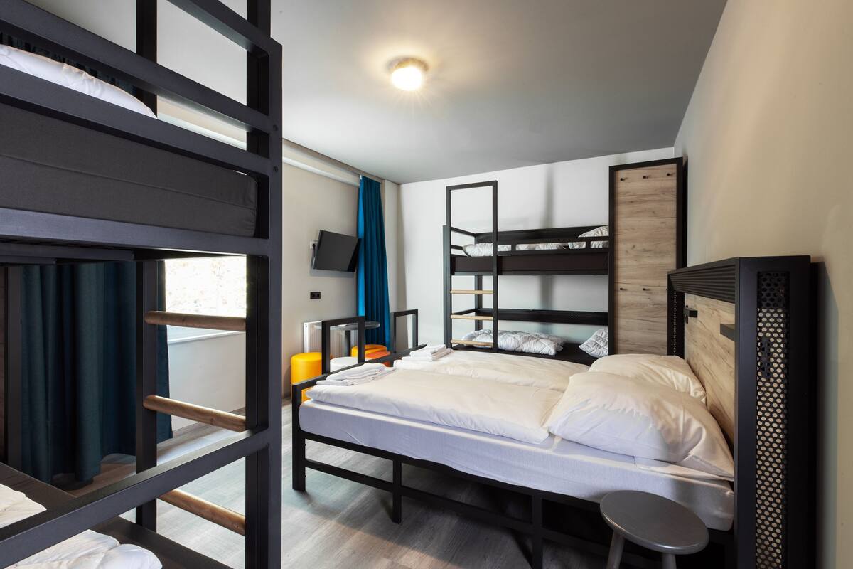 A room with bunk beds, a flat-screen TV, a small stool, and a wooden headboard.