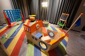 A play area with a colorful striped floor, a wooden ship play structure, a blue and orange toy fence, and a small chalkboard. - Harrys Home Salzburg (Salzburg)
