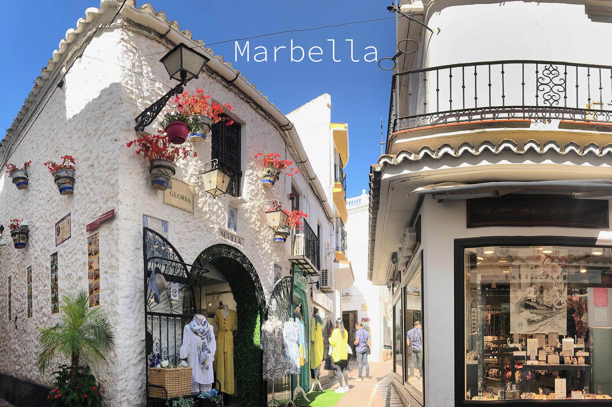 Een smalle straat in Marbella met witte gebouwen, waarvan sommigen balkons en bloempotten hebben.
