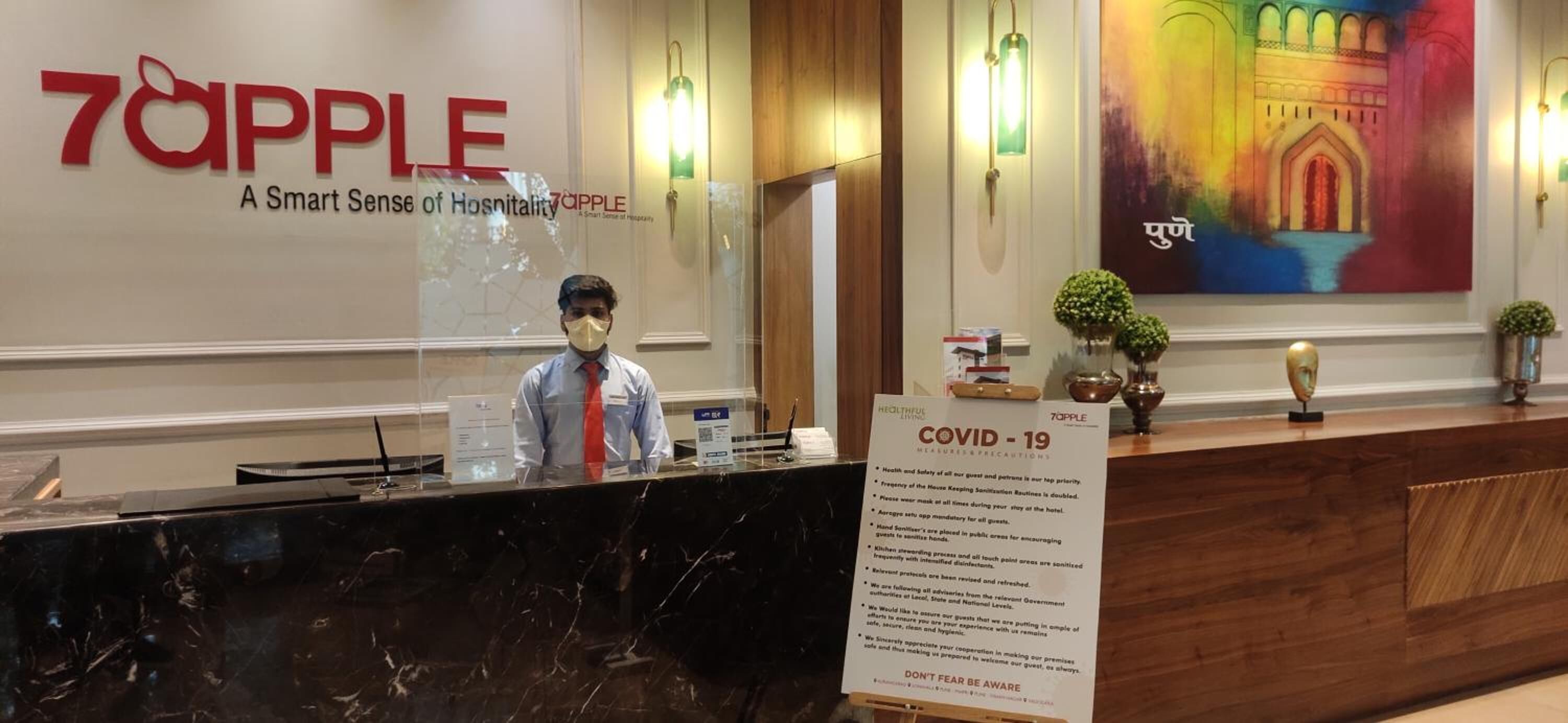 A hotel reception desk with a sign about COVID-19 precautions.