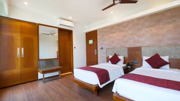 A hotel room with two beds, wooden flooring, a ceiling fan, and an air conditioning unit.