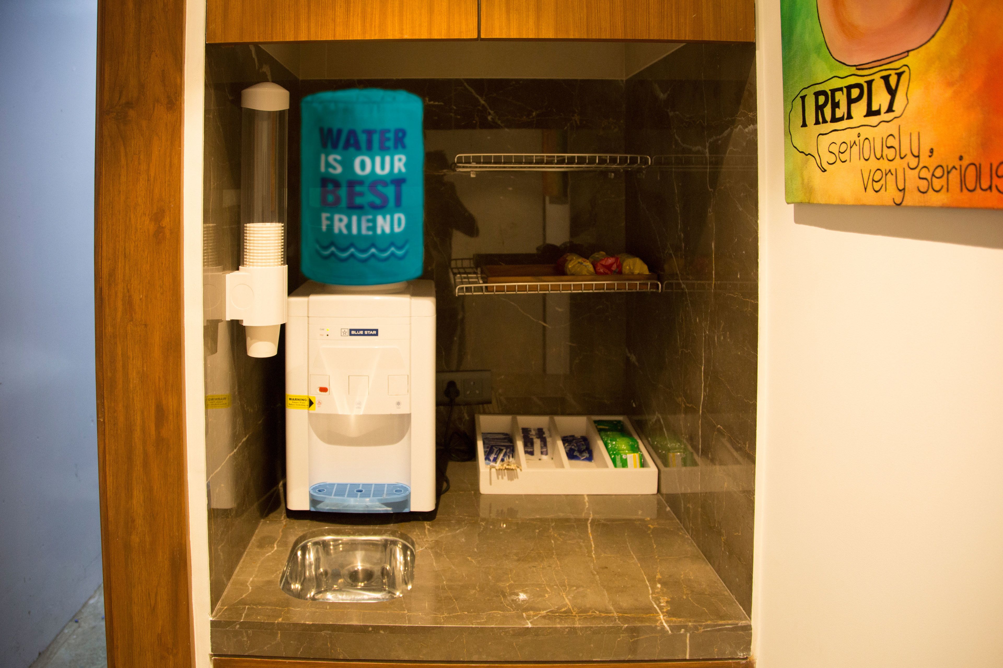 Una kitchenette compacta con dispensador de agua, cafetera y refrigerador pequeño.