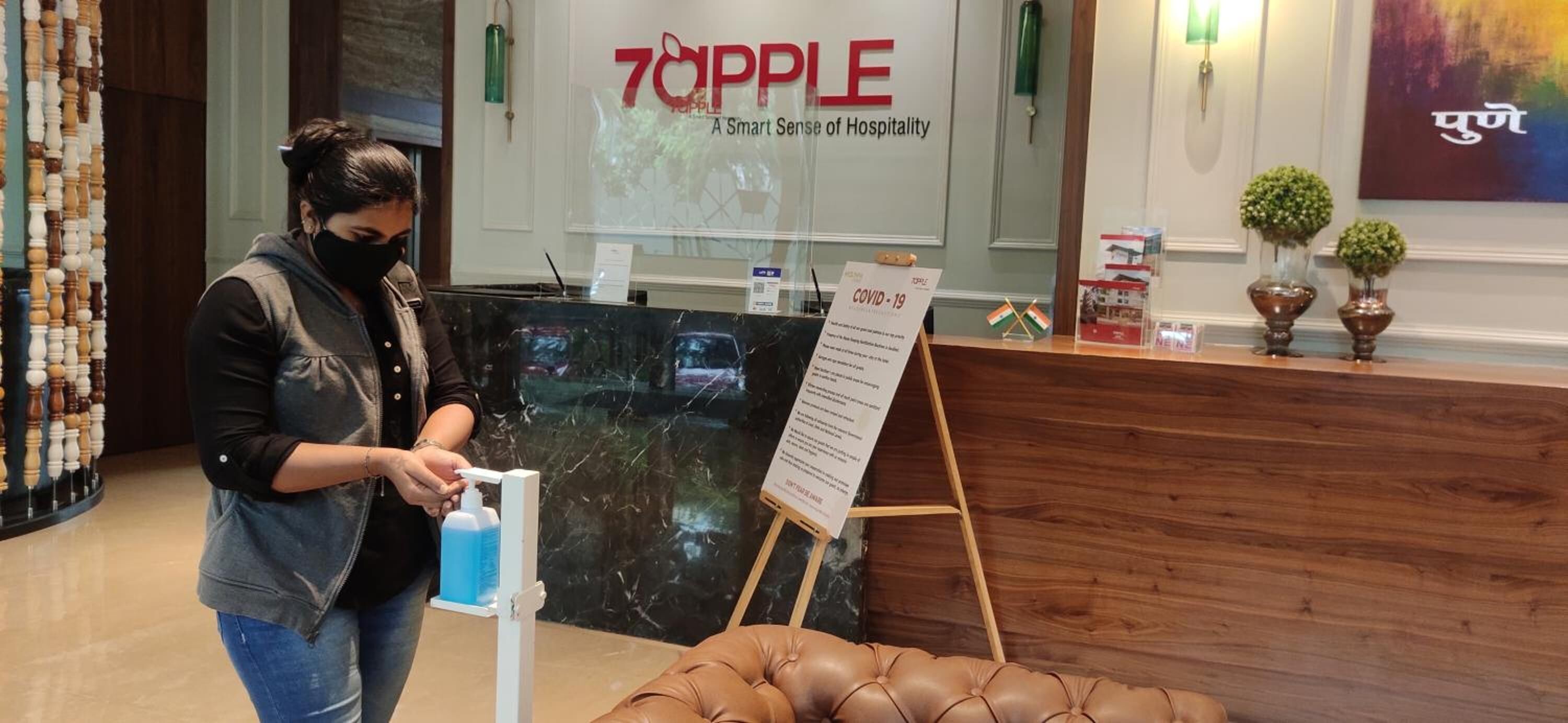 A hotel reception area with a marble counter, a sign reading "70APPLE A Smart Sense of Hospitality", and a COVID-19 information stand.