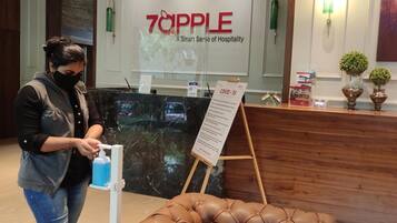 A hotel reception area with a marble counter, a sign reading "70APPLE A Smart Sense of Hospitality", and a COVID-19 information stand.