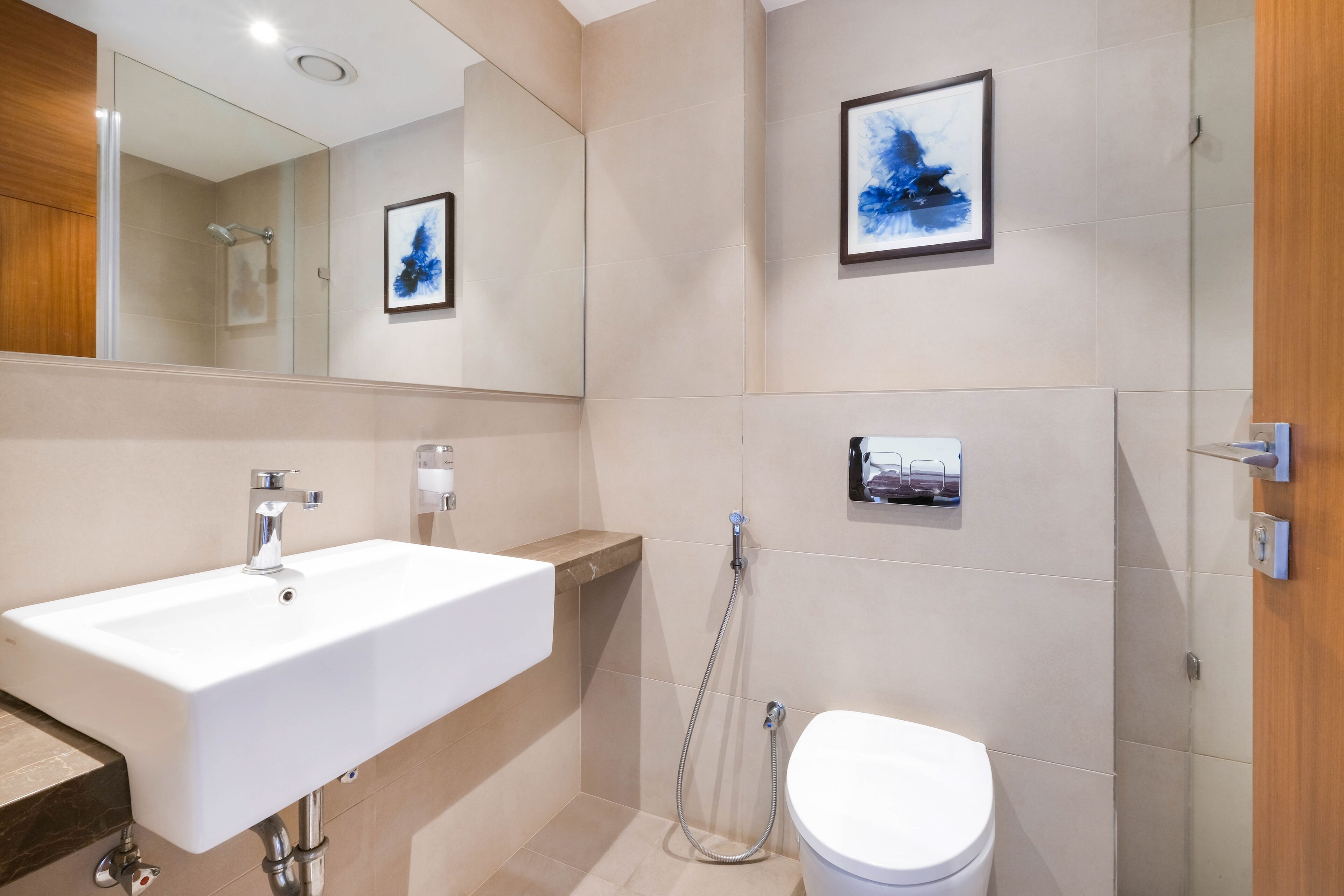 A modern bathroom with a white sink, a toilet, and a shower. There are framed pictures on the wall.