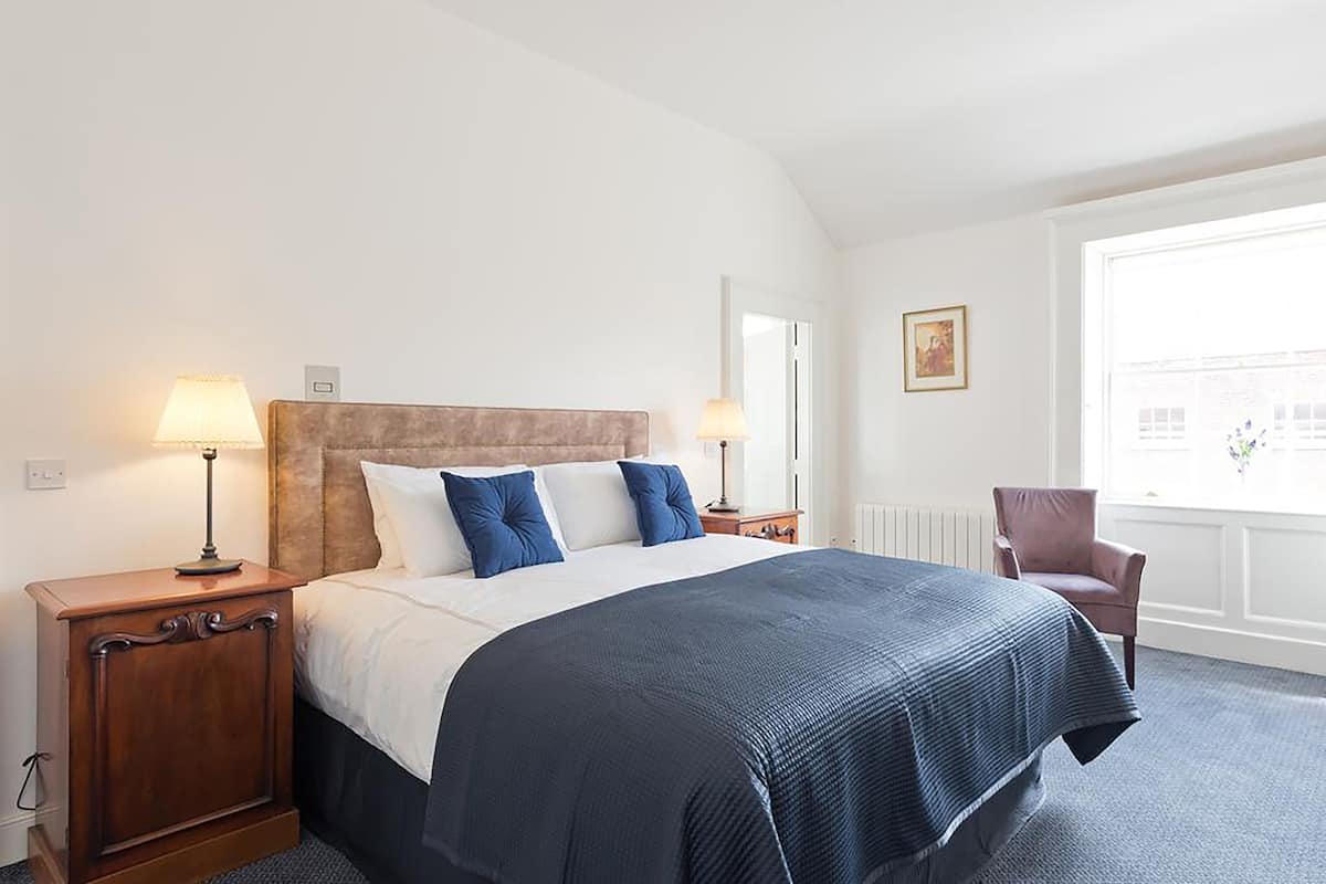 Una habitación de hotel con una cama grande, dos lámparas de noche, una silla y una ventana con vistas.