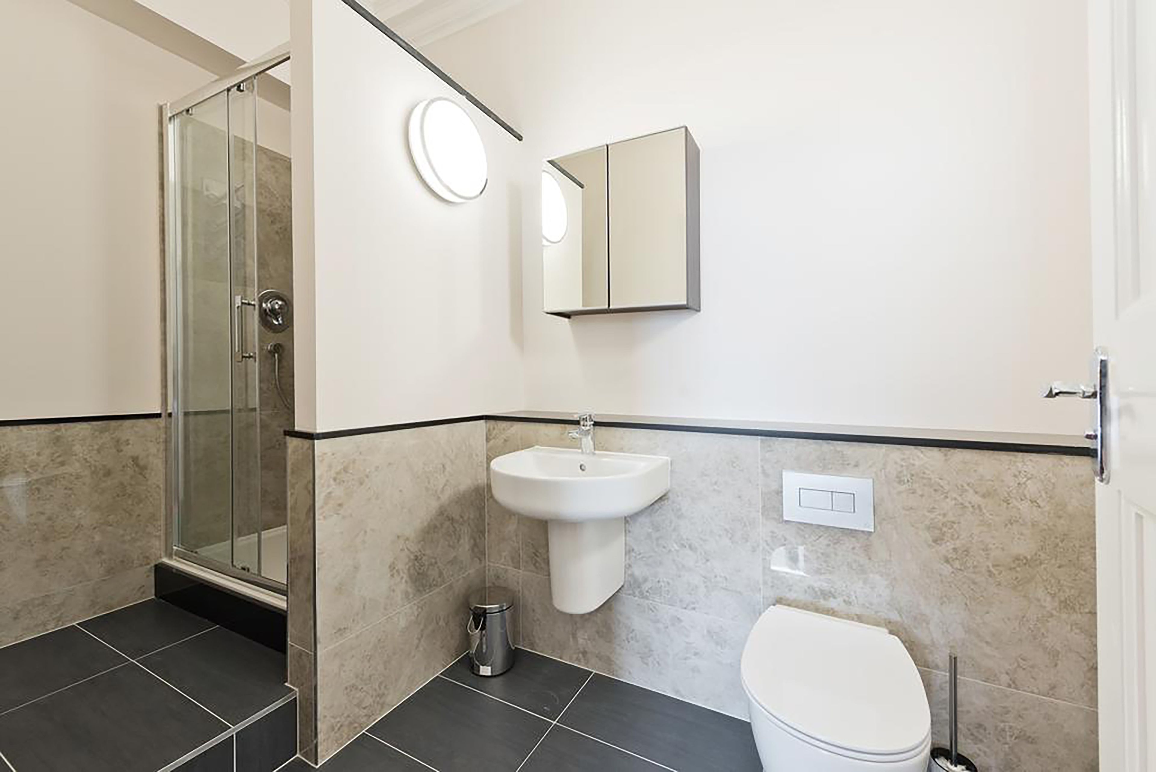 A bathroom with a glass shower enclosure, a pedestal sink, a toilet, and a mirror.