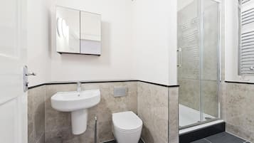 Ein modernes Badezimmer mit einem Waschbecken auf Säule, einer Toilette und einer Duschkabine aus Glas.