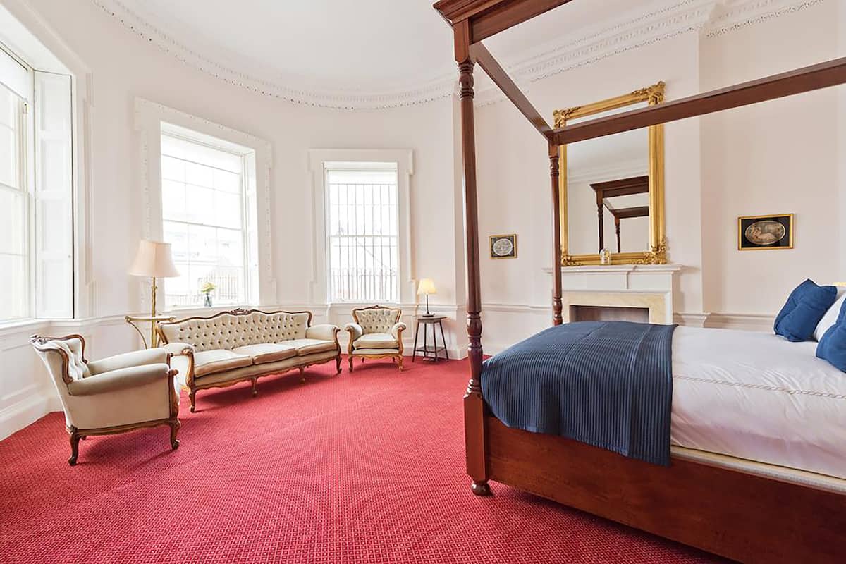 Un dormitorio espacioso con una cama con dosel, una chaise longue y un sofá.
